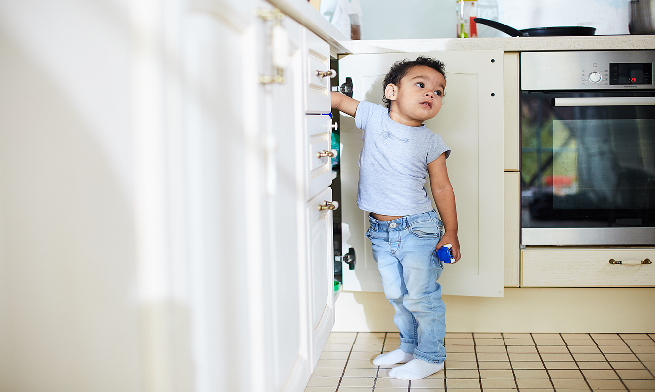 young child reaches into cabinet under sink