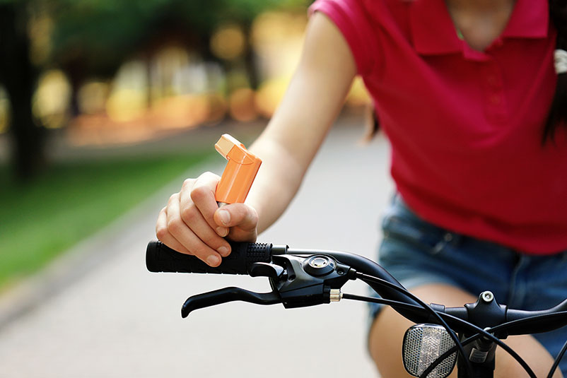 Girl riding a bike holds an inhaler