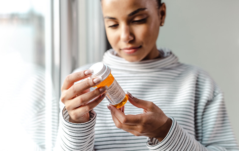 A woman reads the label on a pill bottle.