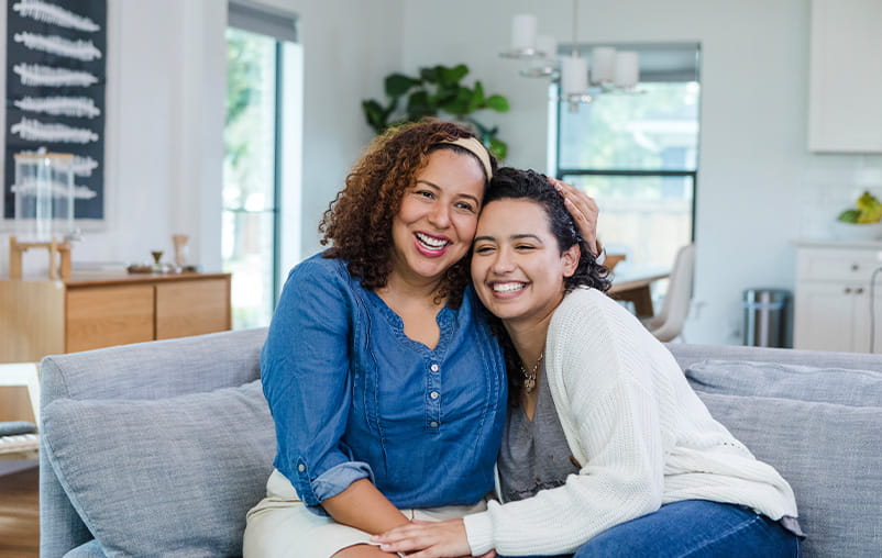 Mother and daughter sit on a couch together, smiling
