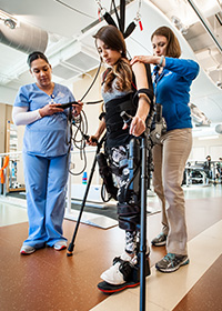 Woman using the EKSO Exoskeleton to walk. Two physical therapists are helping her.