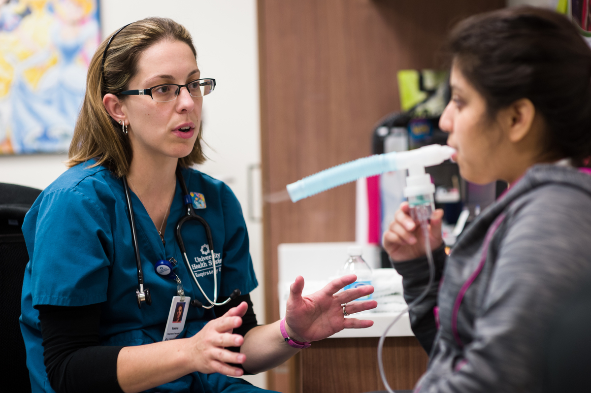 Physician talking to patient while patient inhales asthma medicine.