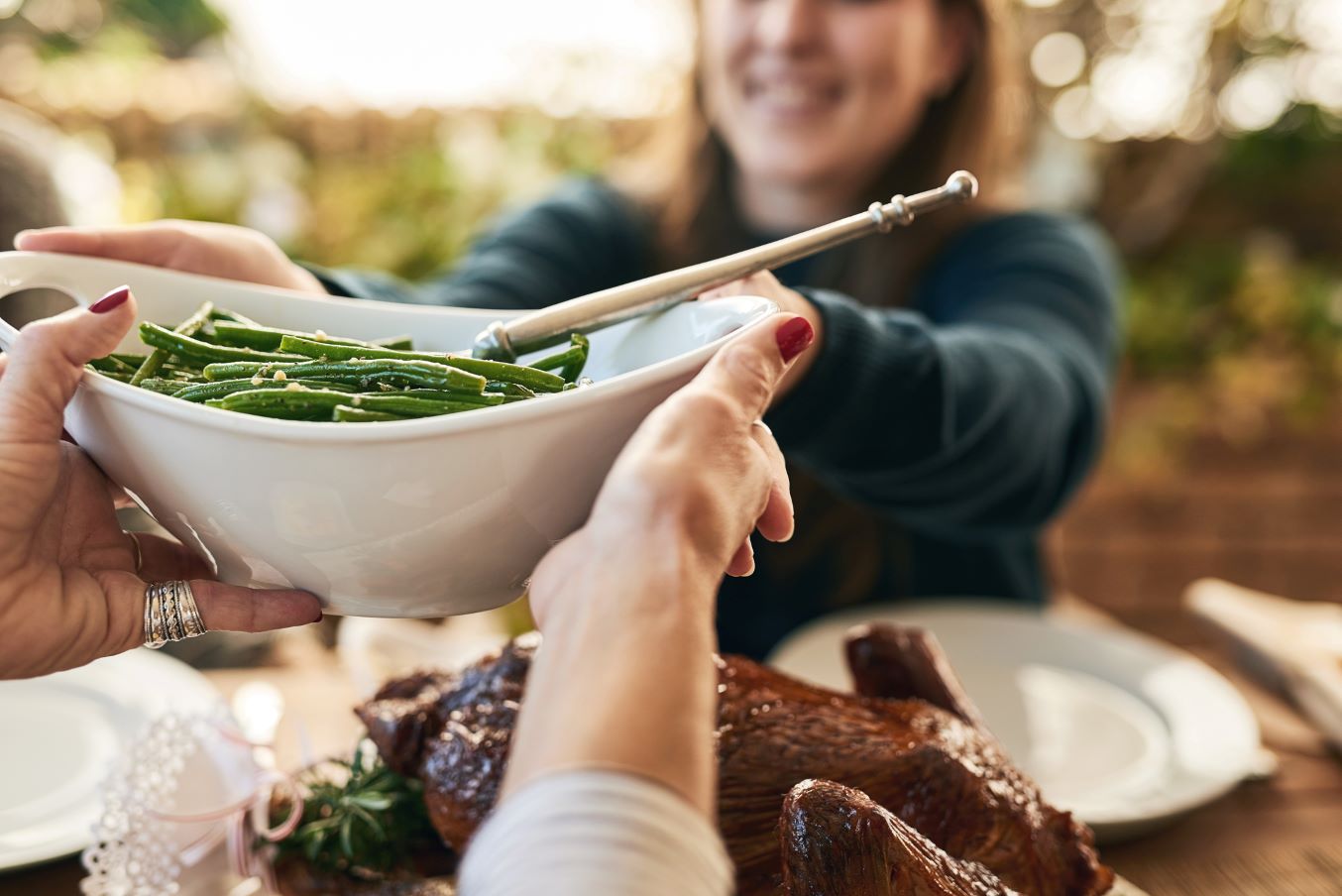 Someone passes a dish of green beans over a Thanksgiving table.