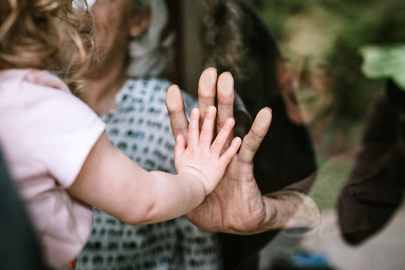 Child and grandparent touching hands through glass