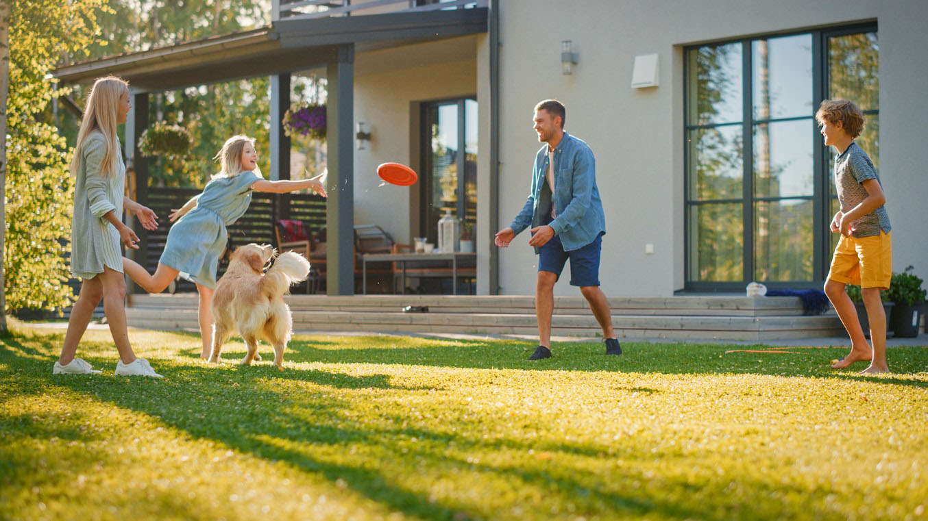 Family plays frisbee in the backyard with their golden retriever.