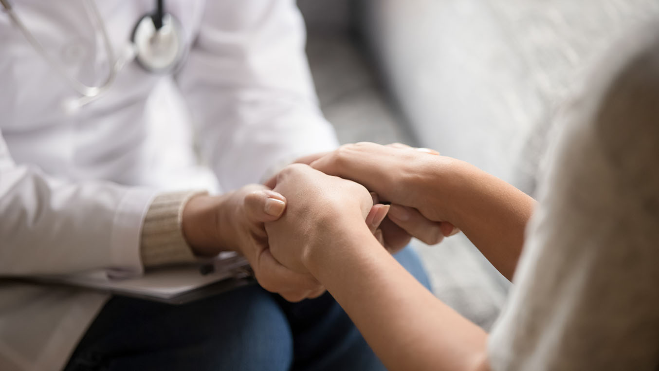 Close-up shot of a health care provider holding the hands of a female patient so show empathy and support.