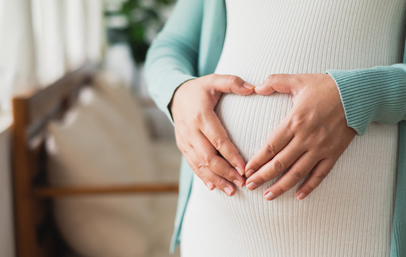 A pregnant woman makes a heart shape with her hands on her belly.
