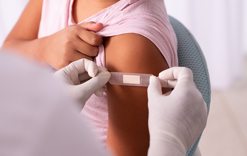 A medical provider puts a Band-Aid on the arm of a child wearing a pink shirt.