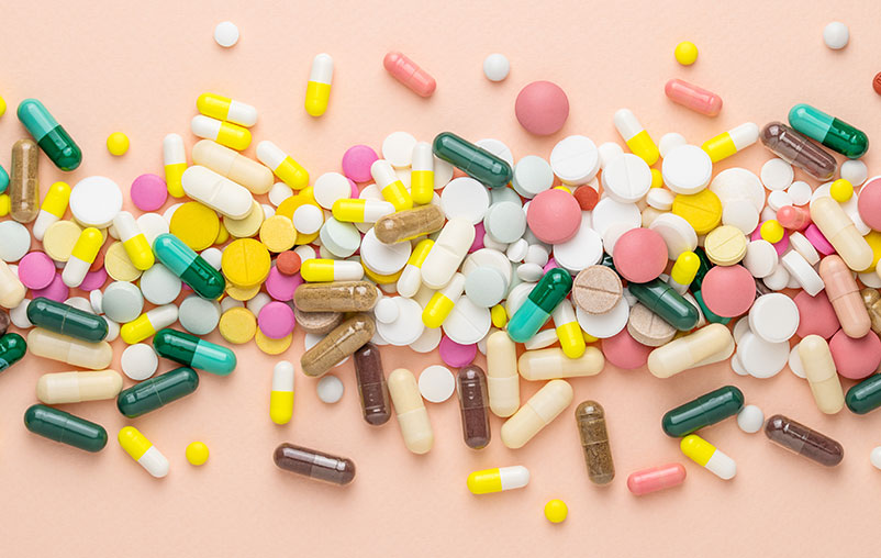 Hundreds of pills of all shapes and sizes laid out on a pink canvas.