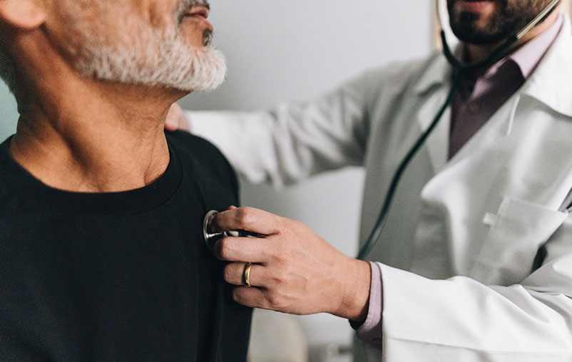 Man with black shirt and gray beard getting heart rhythm checked by cardiologist.