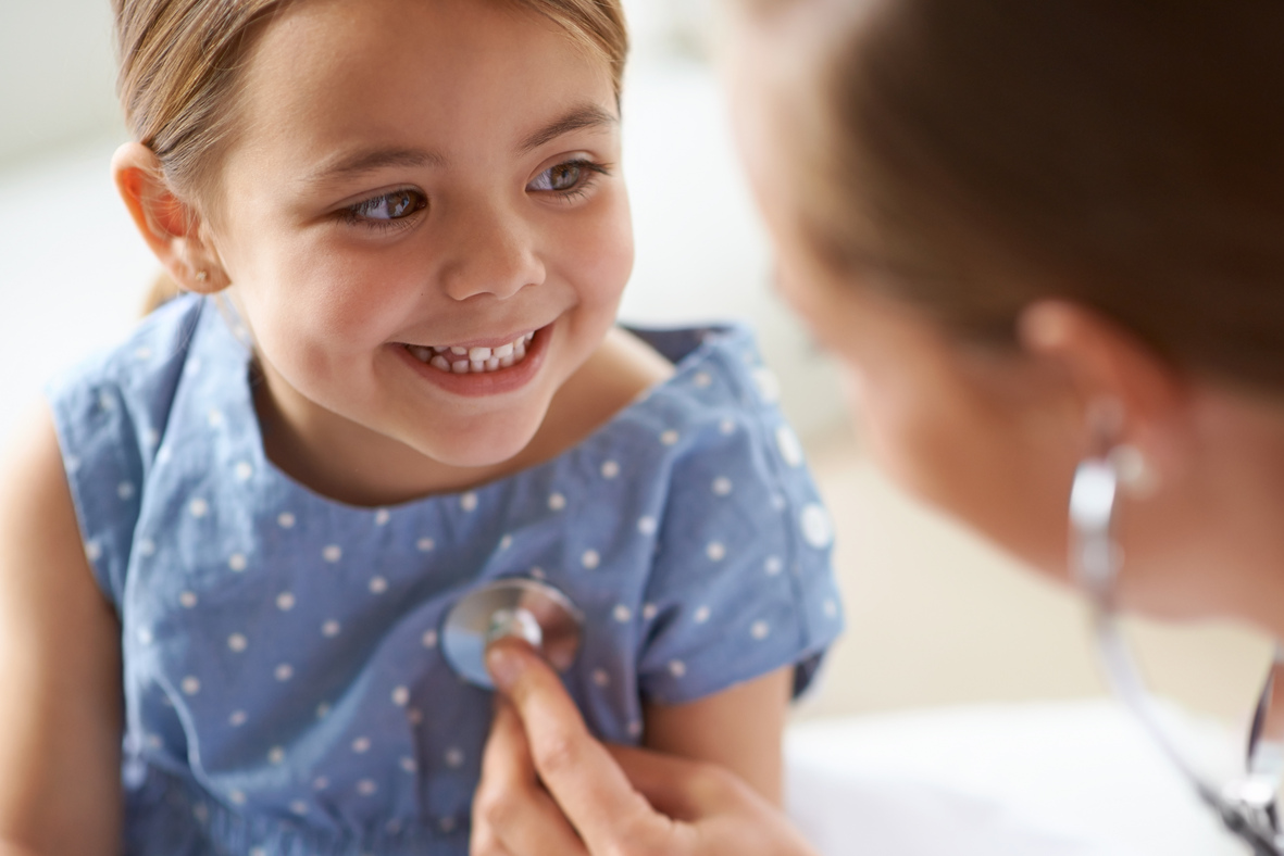 Little girl in a blue polka dot dress and a big smile with her primary care provider getting her heart rate checked.