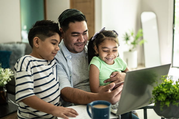 A father and two children look at a laptop.